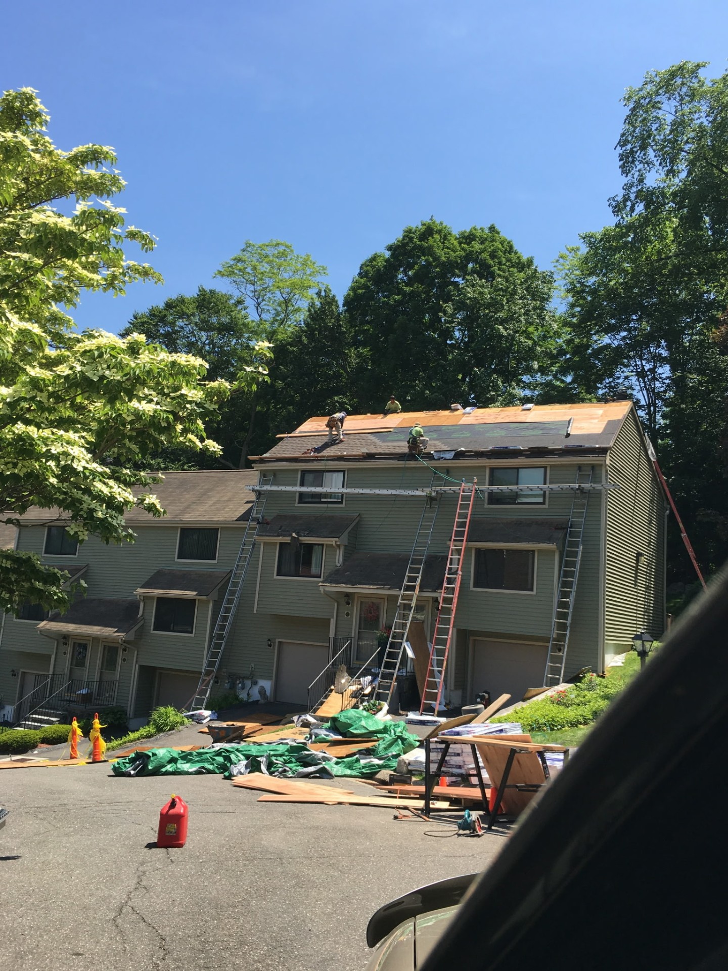 Wide shot of the townhome mid-install with ladders, ground tarps and crew on the roof