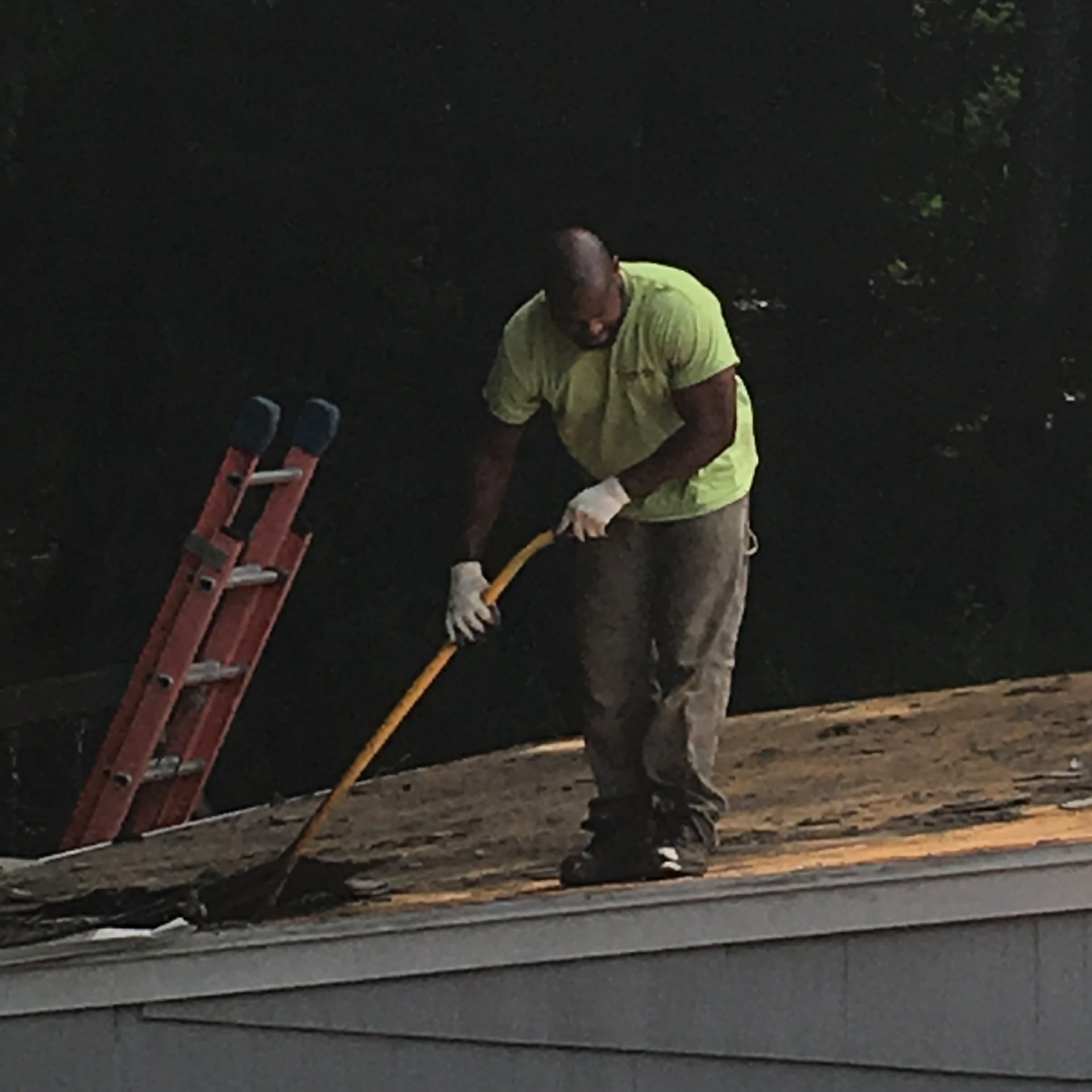 Roofer stripping shingles down to the deck with a tear-off bar