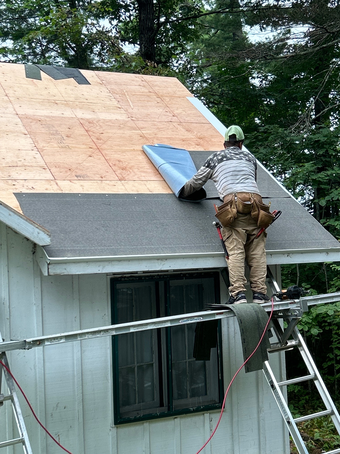 Roofer rolling out ice-and-water shield along the eave of the cottage