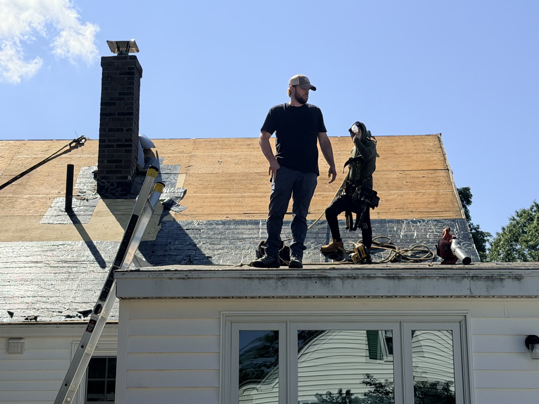Crew standing on the stripped roof with fresh plywood sheathing installed across the upper slope