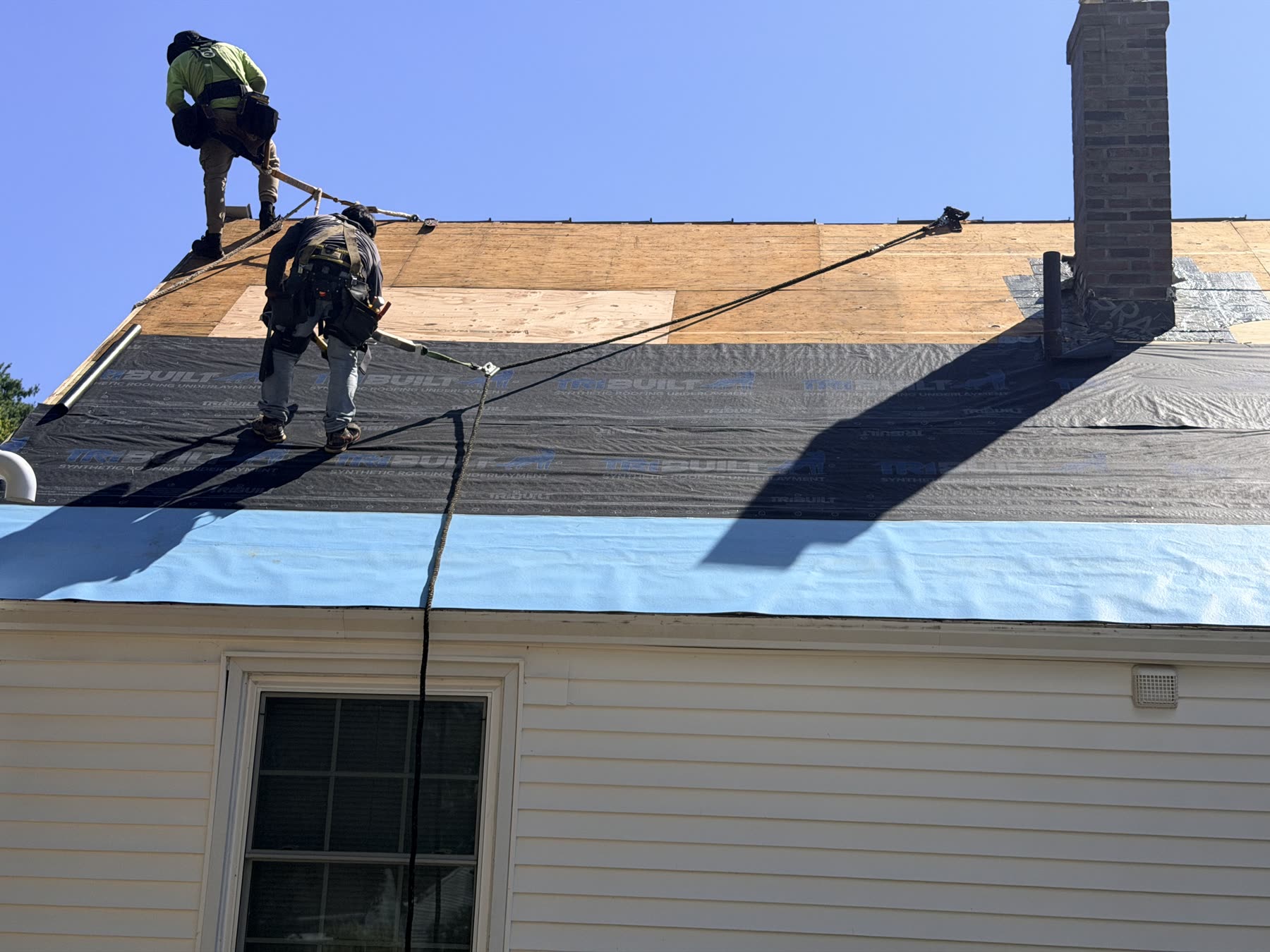 Roofers working on the roof as synthetic underlayment is rolled over new plywood decking