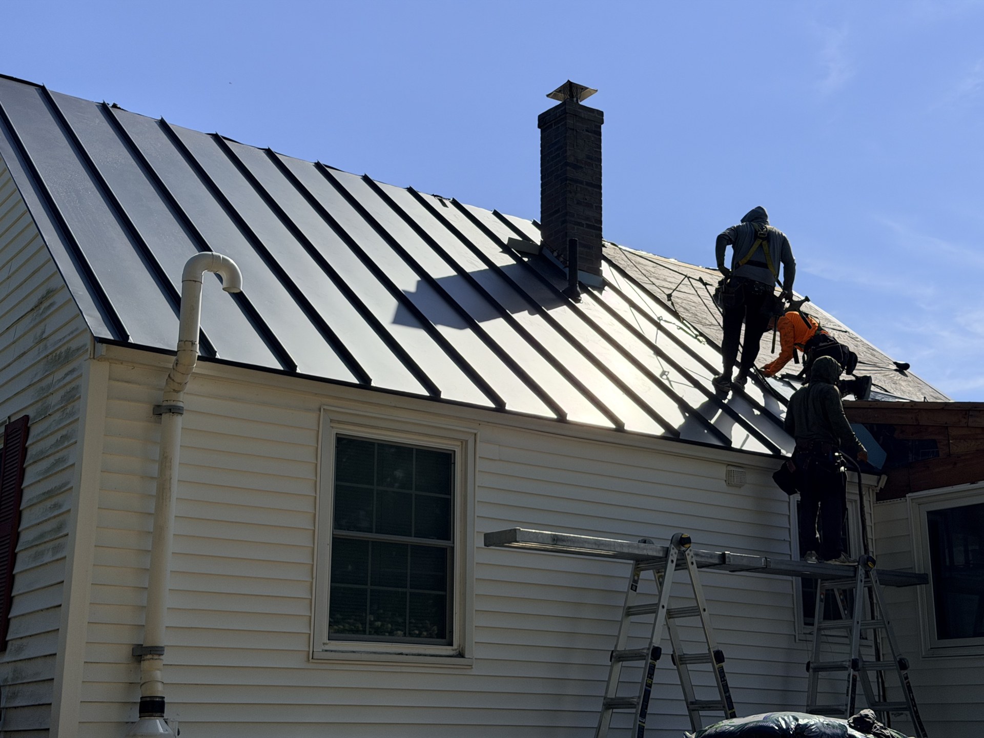 Standing-seam metal panels installed around the brick chimney with crew working the far slope