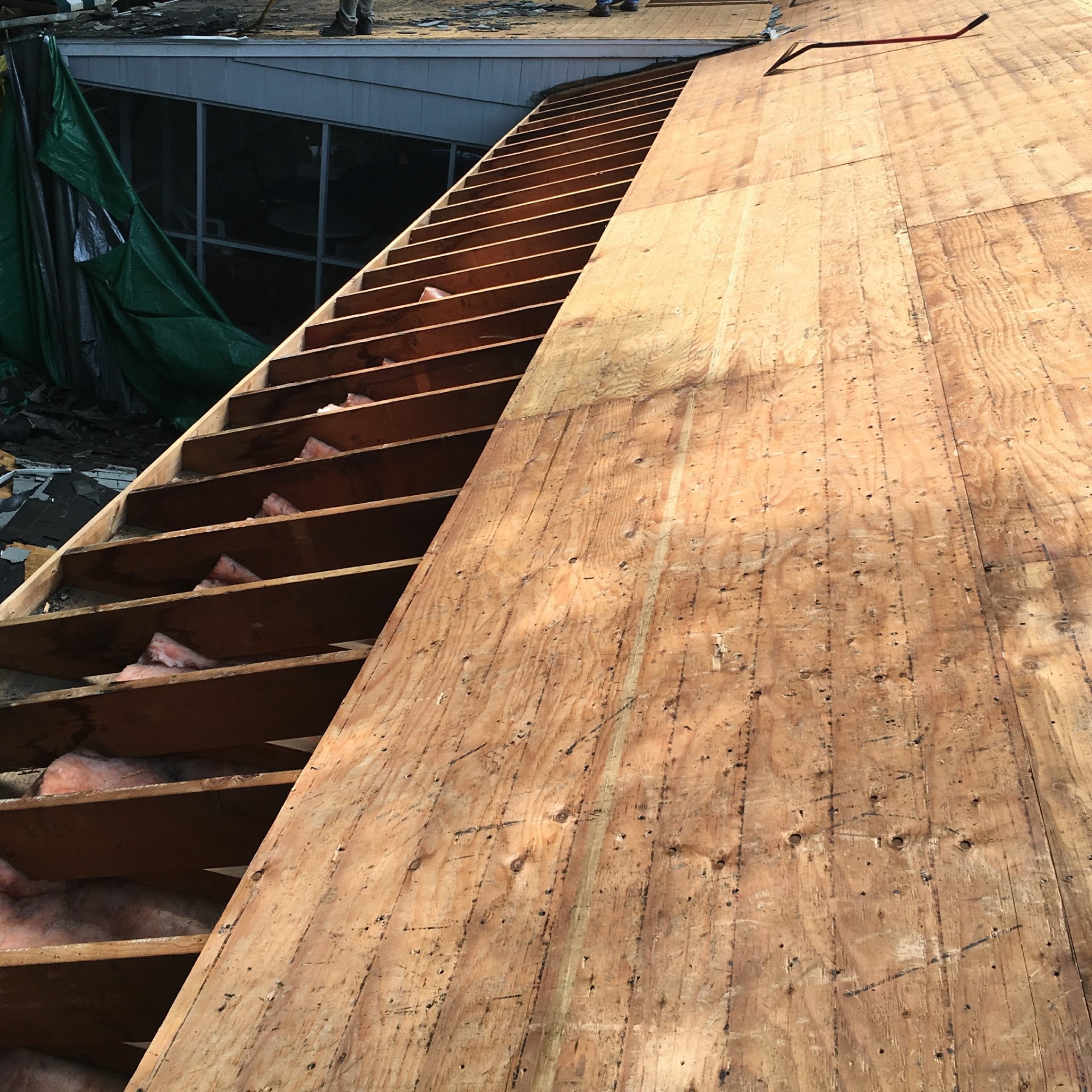 Section of plank sheathing removed exposing rafters and pink insulation