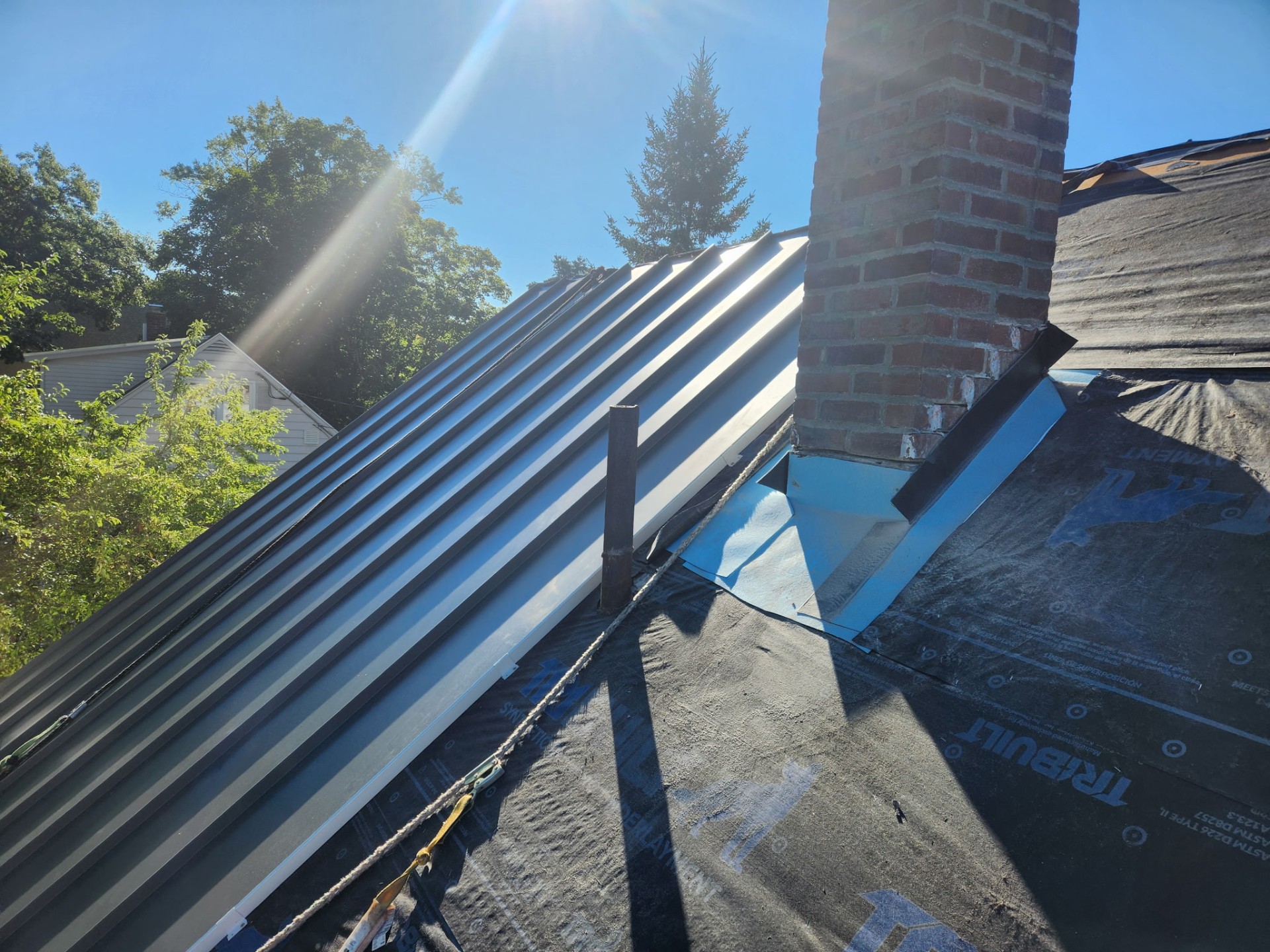 Standing seam panels meeting new step flashing around the brick chimney over synthetic underlayment