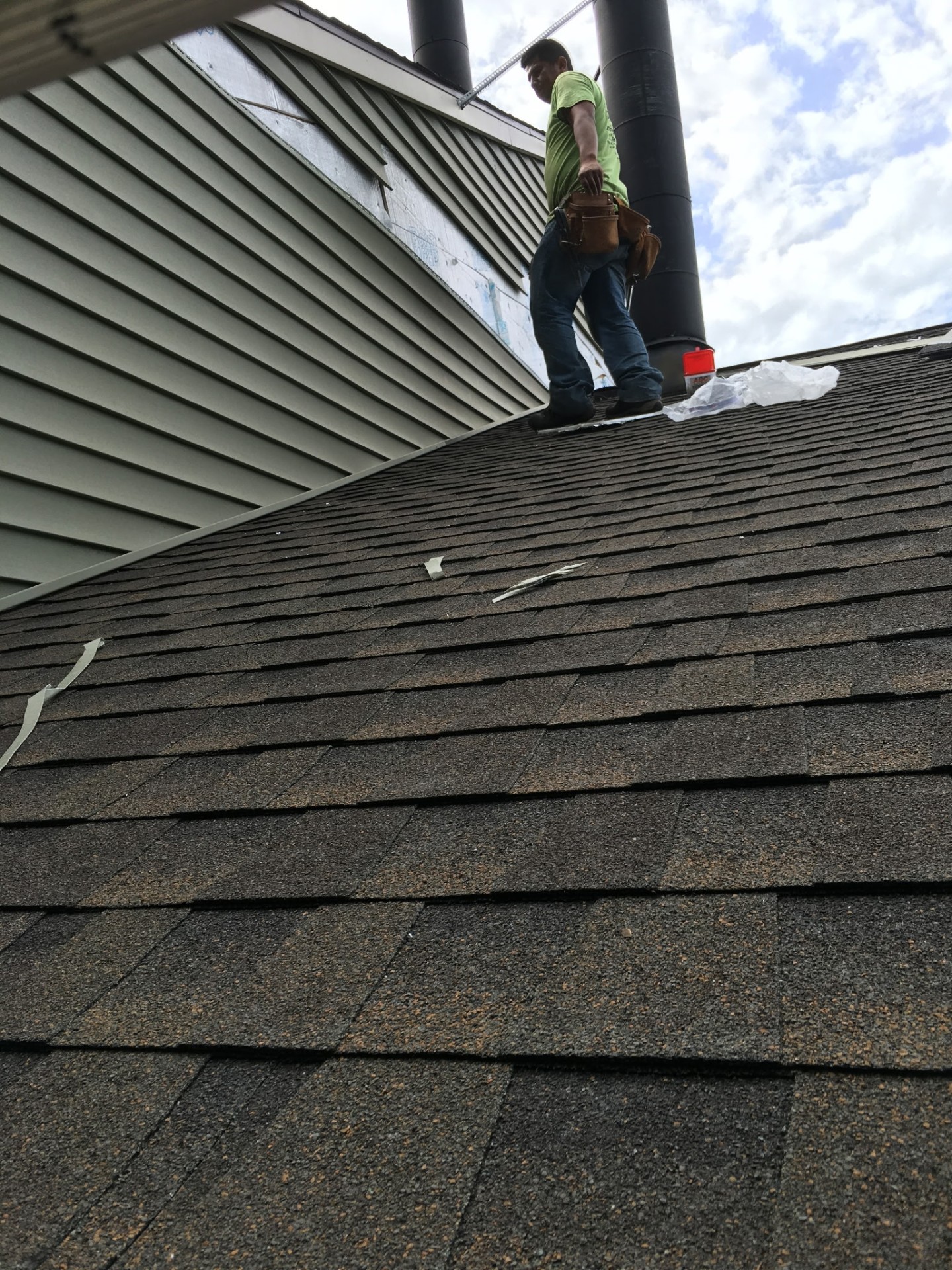 Roofer working around a metal chimney flue on freshly-laid shingles