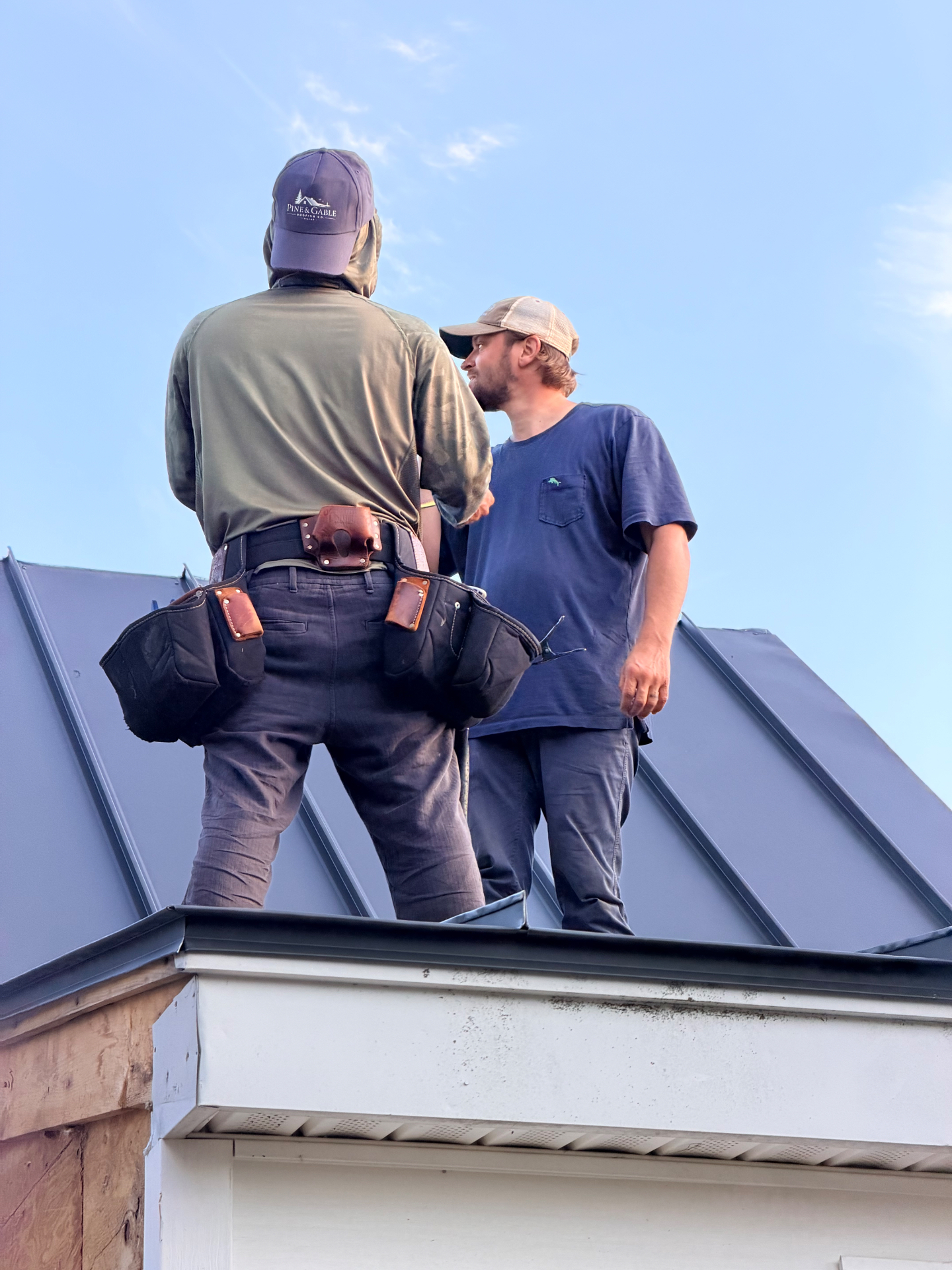 Two Pine & Gable roofers talking over ridge details on the finished standing seam roof