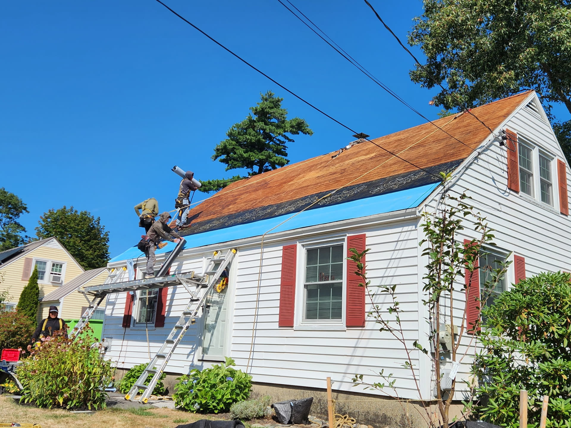 Crew rolling out underlayment across the bare roof deck from ladders and planks