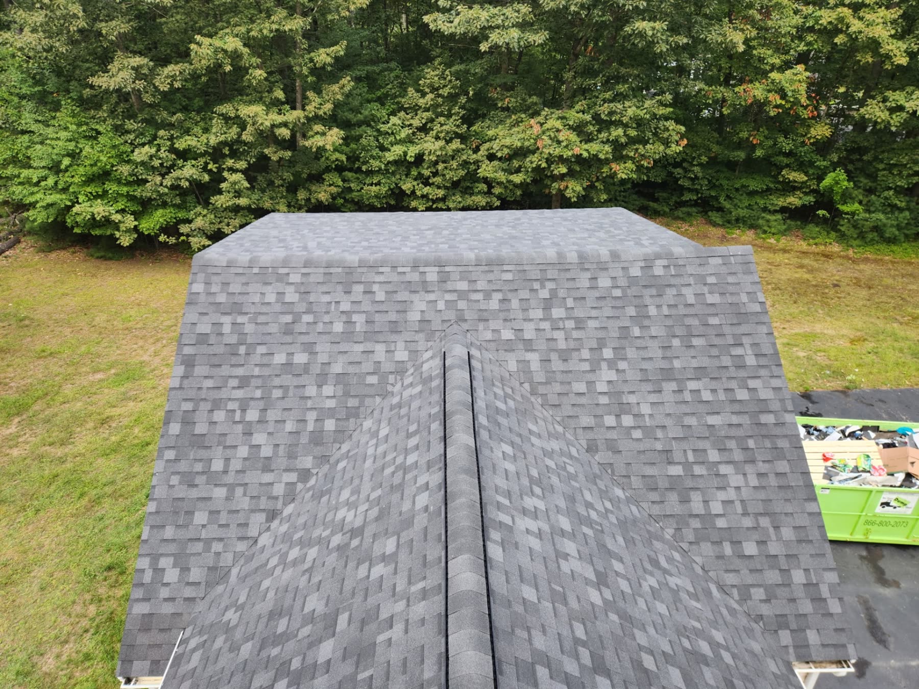 Finished shingle slope on the Wells home with the dumpster being loaded below