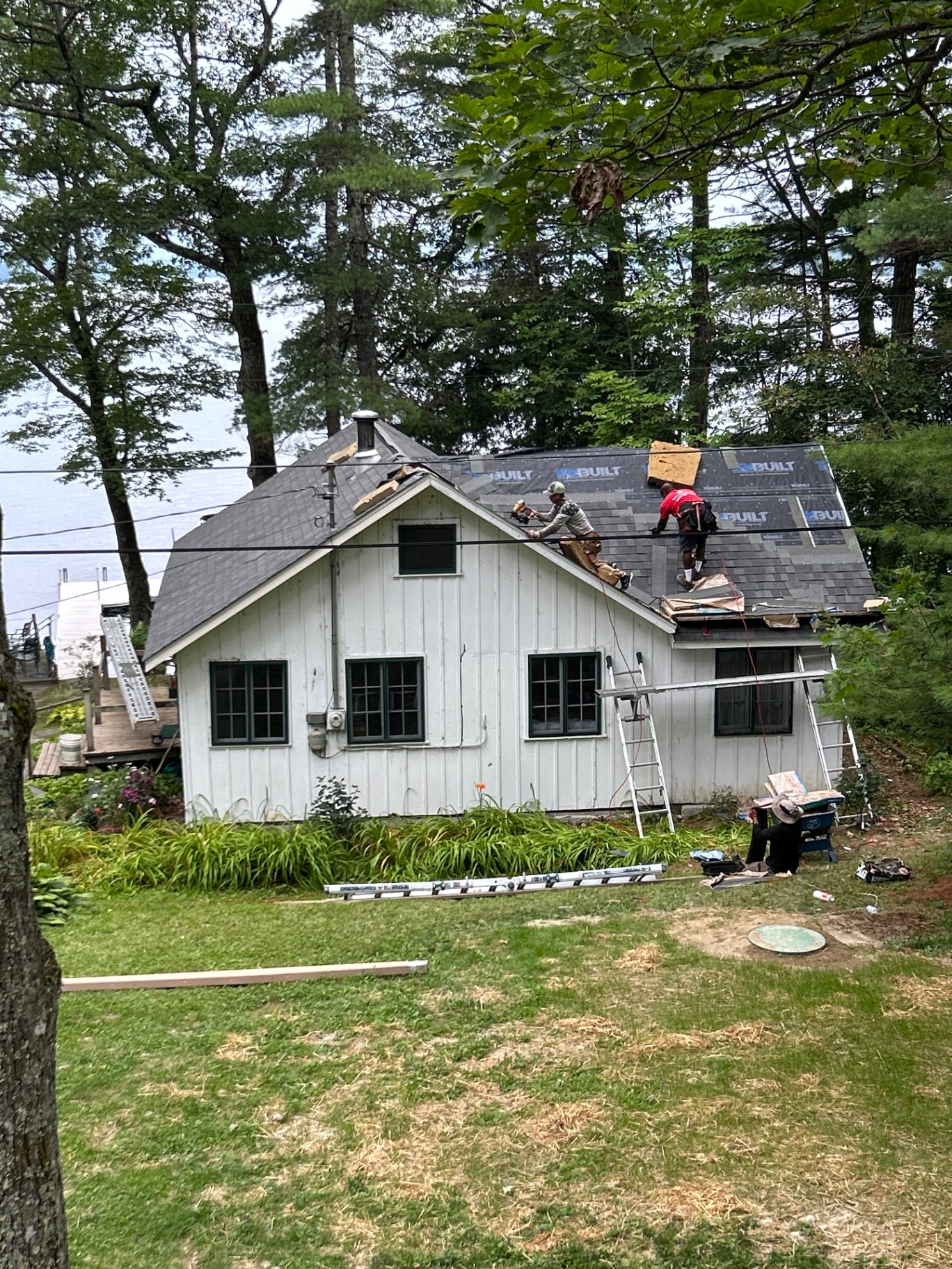 Two roofers nailing new architectural shingles on the cottage with the lake visible behind
