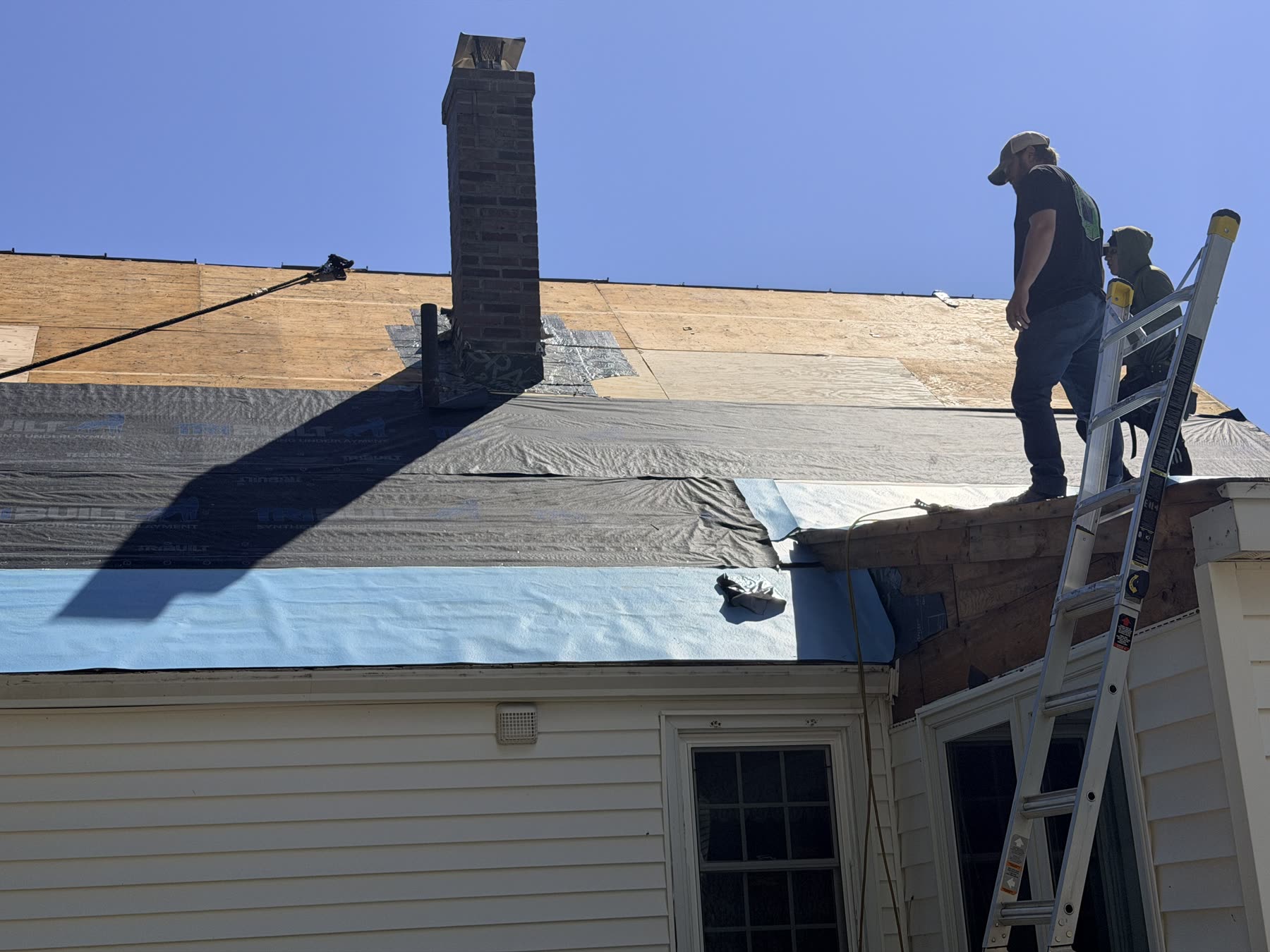 Underlayment and eave membrane installed up to the brick chimney with crew on the ridge