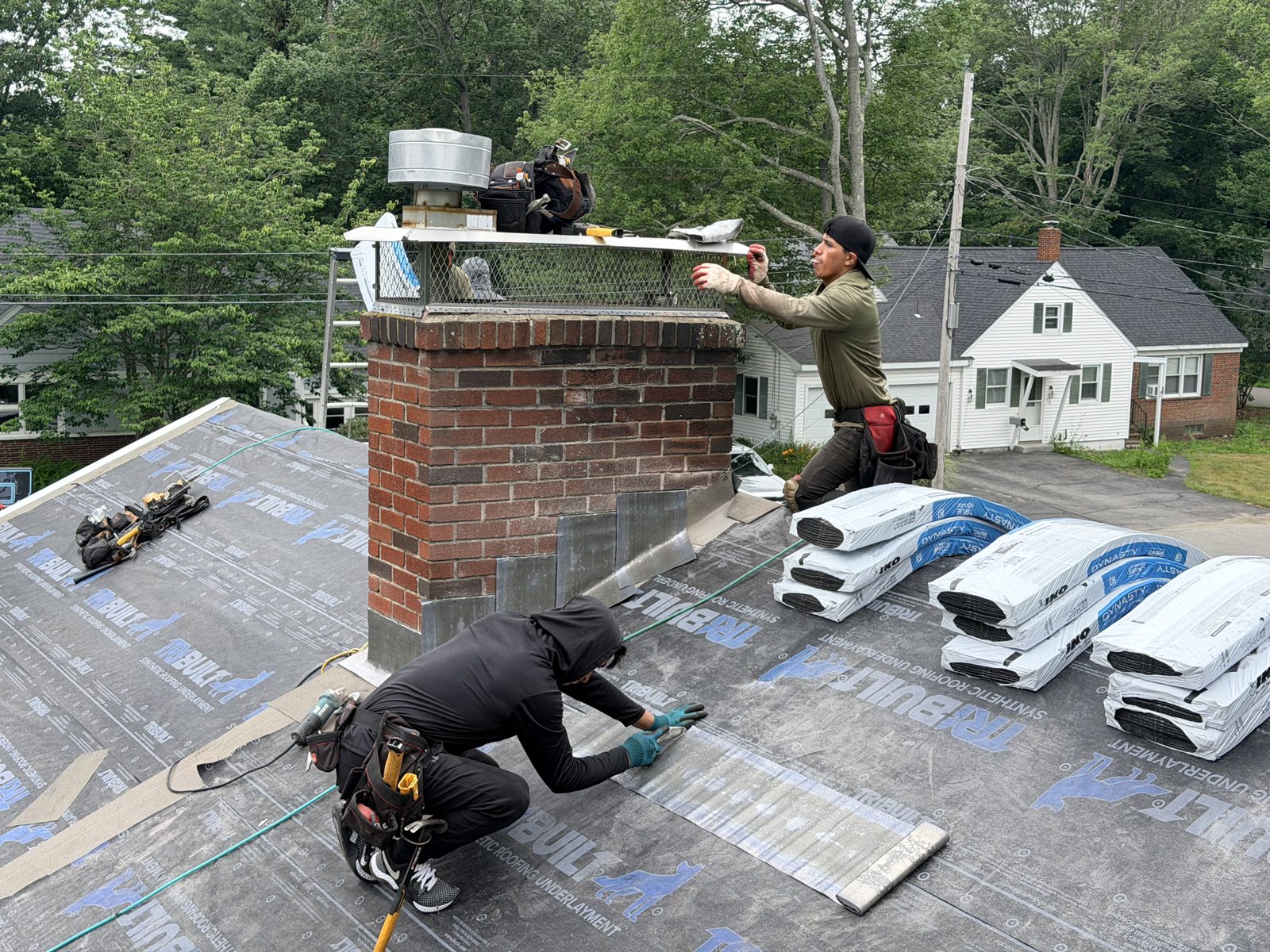 Roofer flashing the brick chimney on fresh underlayment