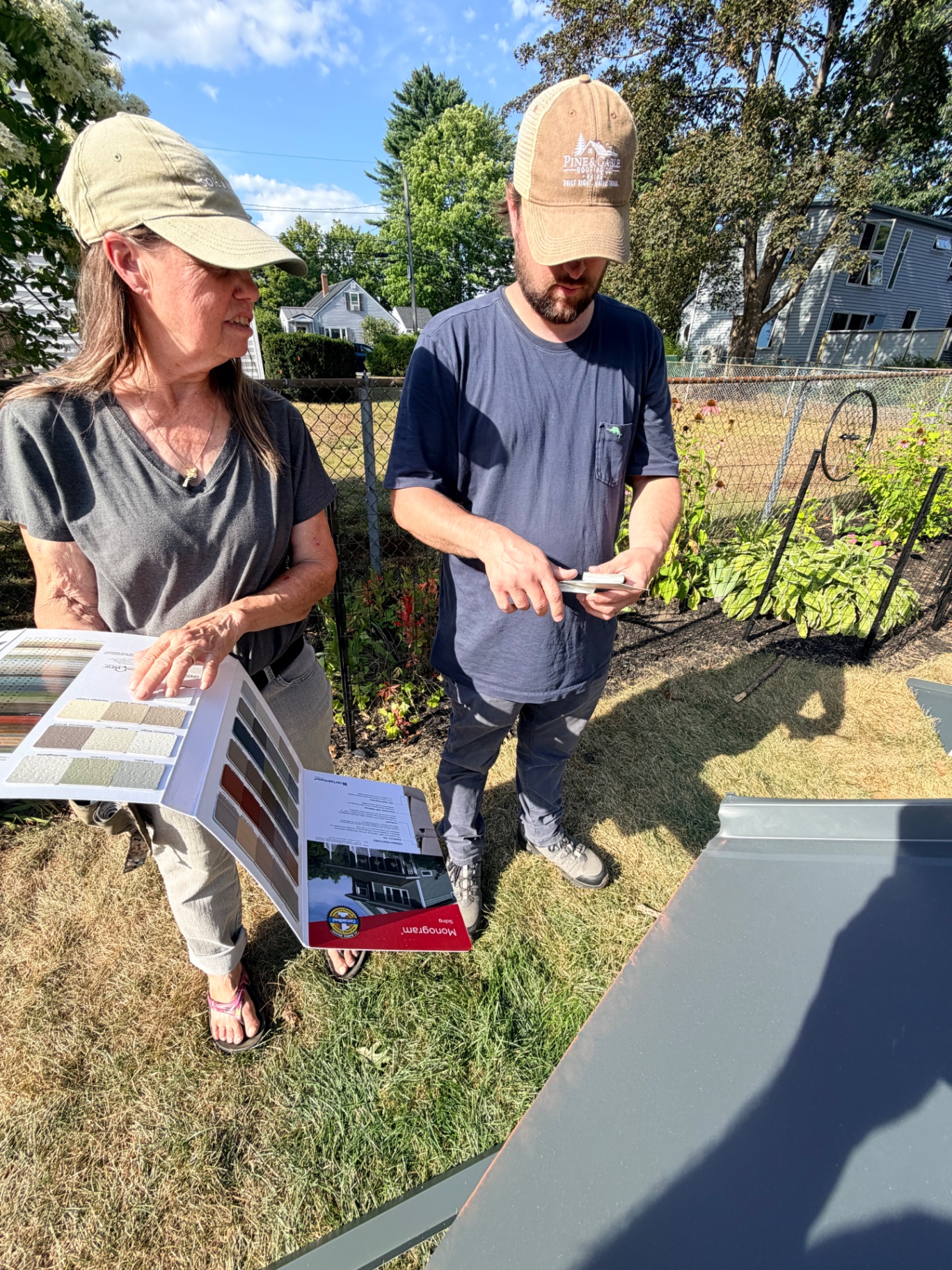 Pine & Gable estimator reviewing Drexel metal color samples with the homeowner in the yard